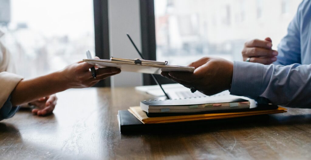 pexels photo 5673502 5673502 Crop anonymous ethnic woman passing clipboard to office worker with laptop during job interview